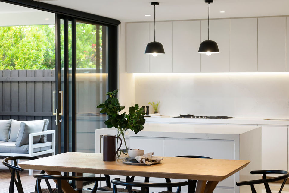 Modern kitchen design with wooden dining table and black pendant lights.