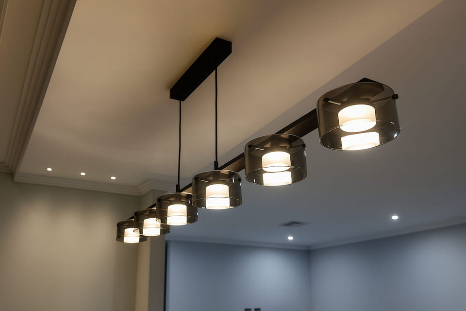Modern pendant lighting fixture with six lights hanging from a black bar.