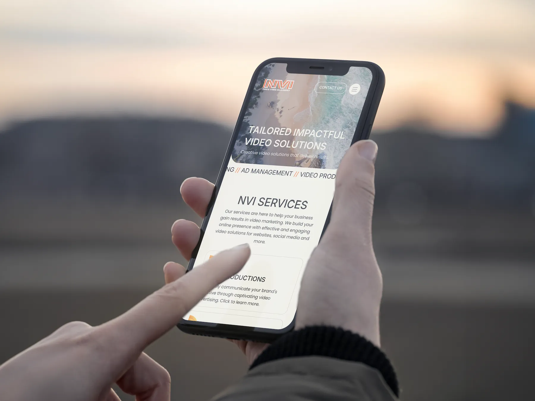 Person using a smartphone displaying the Nice Vibe Imagery mobile website, with a finger interacting with the services section on screen.