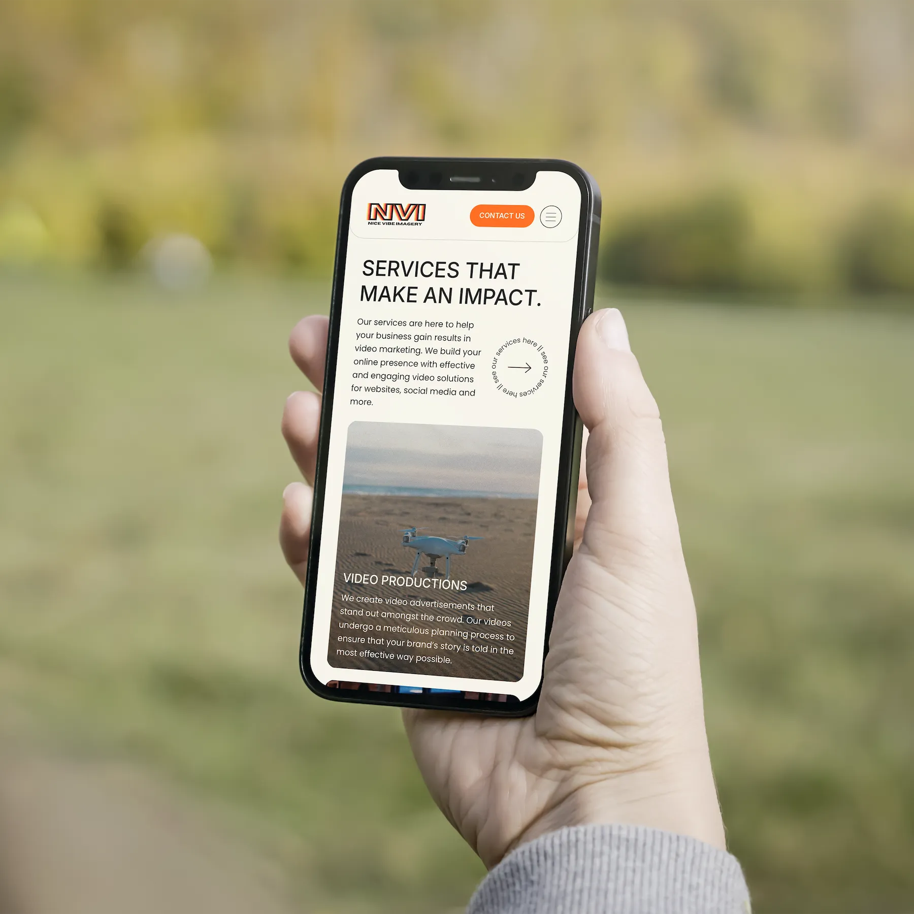 Close-up of a person holding a phone displaying the mobile version of the Nice Vibe Imagery website outdoors.