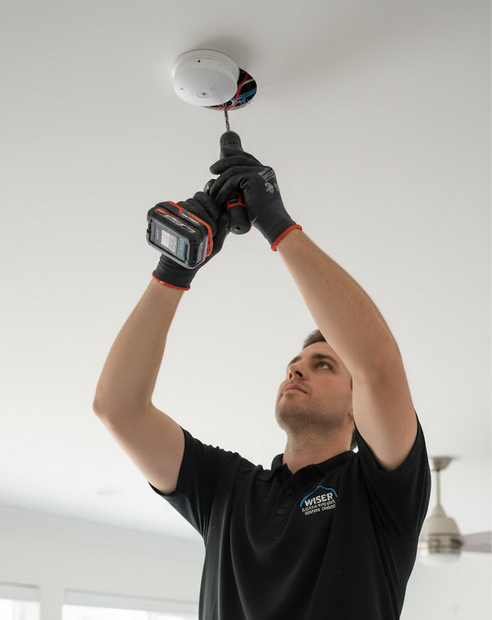 Electrician installing a smoke detector on a ceiling, Wiser Electrical Services visible.