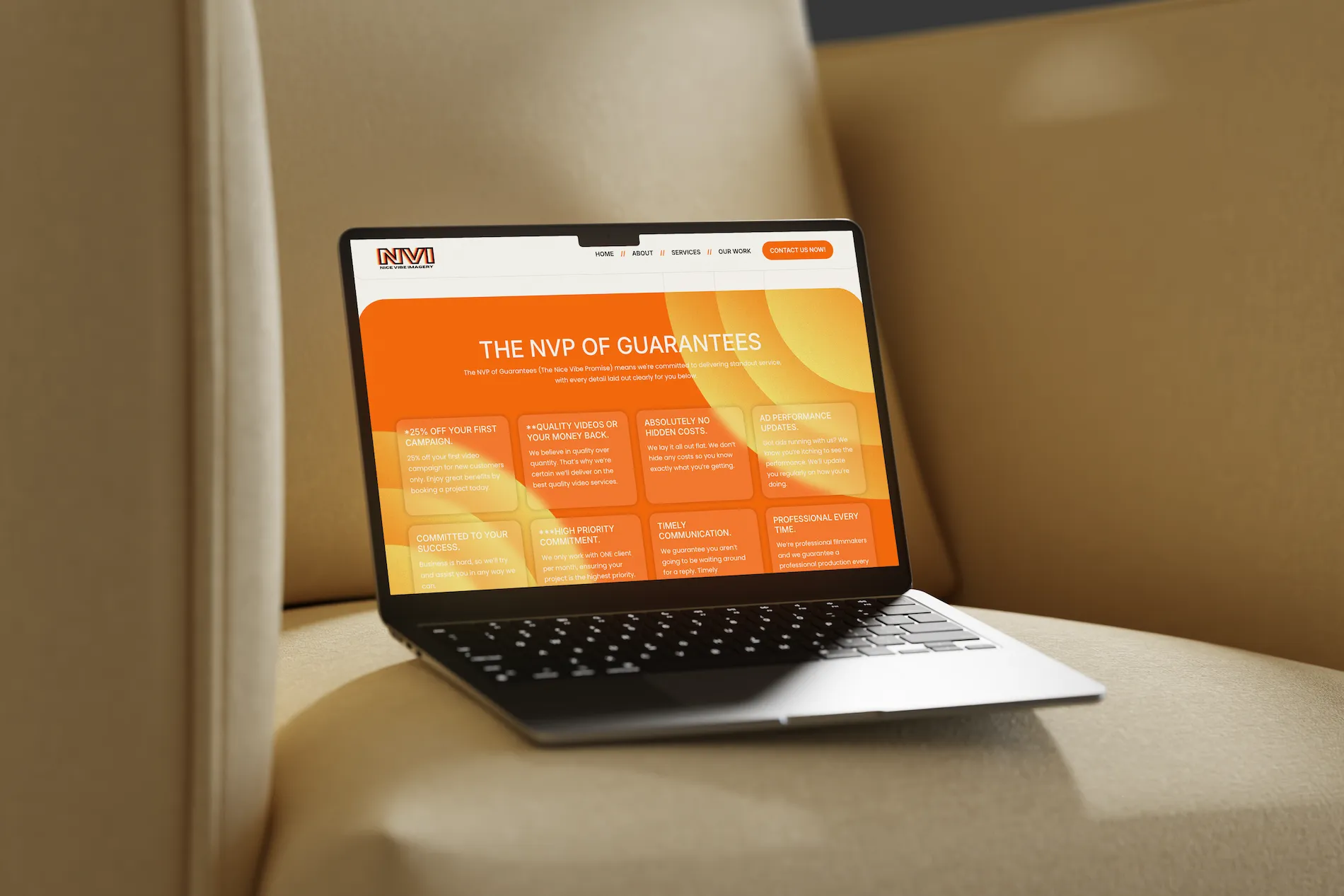 Laptop mockup showing the orange-toned services page of the Nice Vibe Imagery website, set on a beige armchair in soft lighting.