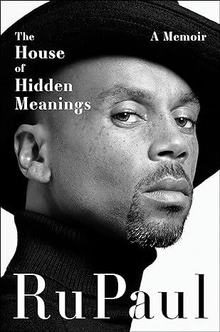 a black and white portrait of RuPaul with a goatee wearing a dark turtleneck and hat tilted to one side as he's facing the left and has his head turned to look at the camera.