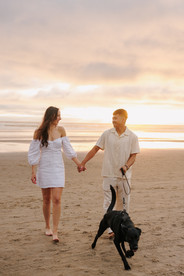 Couple holding hands and walking dog in the sunset at Cannon Beach for engagement photography