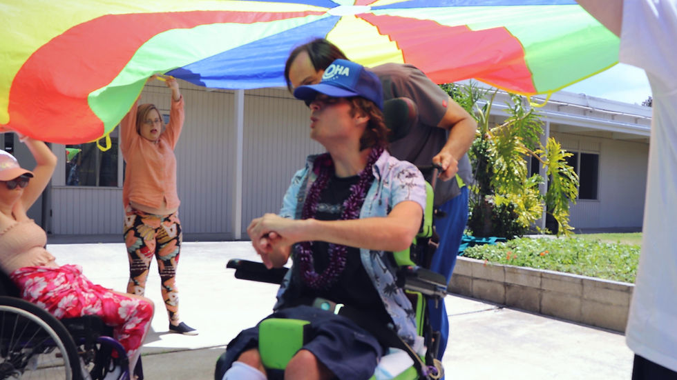 Joshua Andrews in center in wheelchair being assisted by staff under colorful parachute at San Diego Able ARTS Work