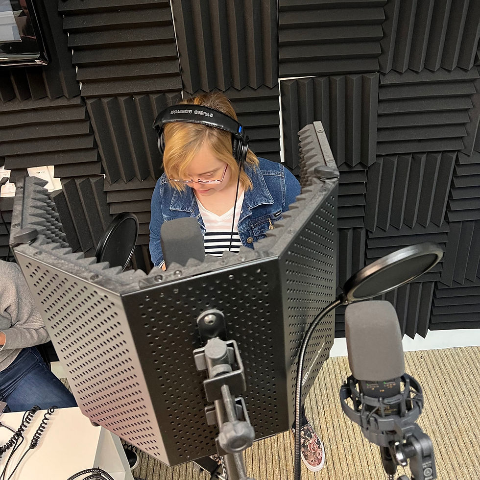 Claire Feth in the recording booth San Diego Able ARTS Work. She is wearing a jean jacket and white shirt. She looks downward with headphones.