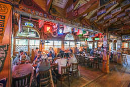 Inside a busy restaurant, people sit at tables; Flags and decorations