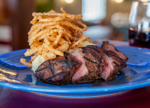 Grilled steak and onion rings served on a blue plate at The Kill Devil Grill