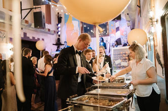 Guests serving themselves food at a catered wedding reception with large balloons.