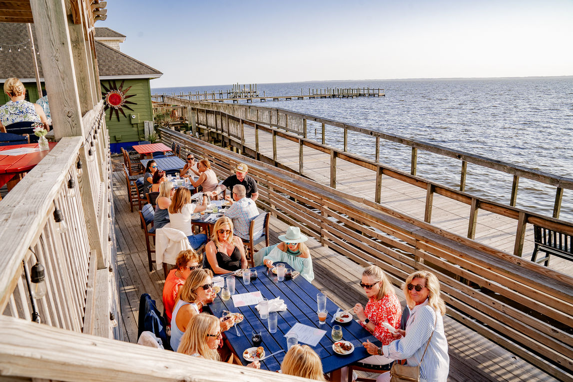 Outdoor dining at NC Coast Grill & Bar with water views and diners.
