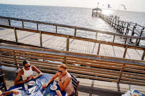 Two women seated at a table, pier, sound view, at NC Coast Grill & Bar.