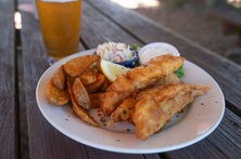 Fried fish plate with potato wedges, coleslaw, and dipping sauce.