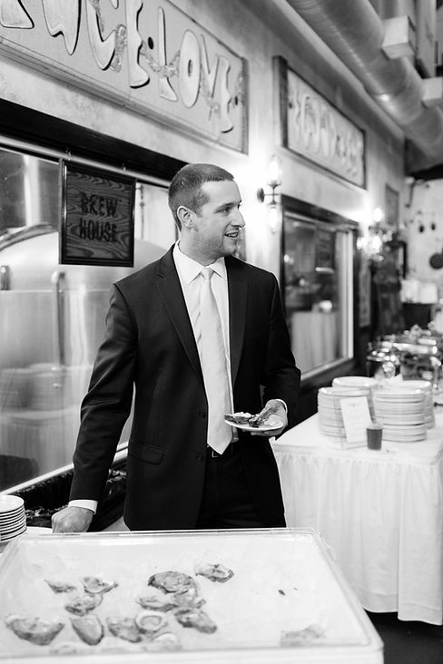 Man in suit stands near food display; catering event in restaurant setting.