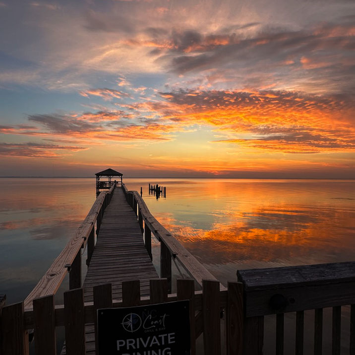 Wooden pier extends into calm water under vibrant sunset sky.