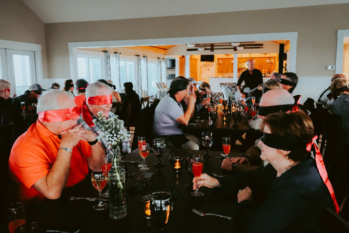 Blindfolded diners at a formal dinner party, enjoying a culinary experience.