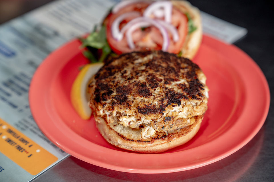 Crab cake sandwich with onion, lettuce, and tomato on a plate. Fat Crabs
