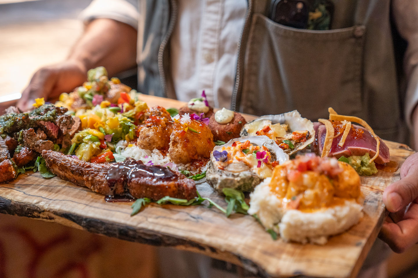 A wooden platter with diverse food dishes at NC Coast Grill & Bar