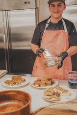 Chef smiling at camera, holding food, three plates. Catering Gallery