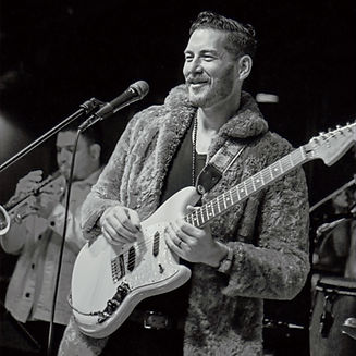 Singer-songwriter plays guitar and sings on stage with a full horn section playing