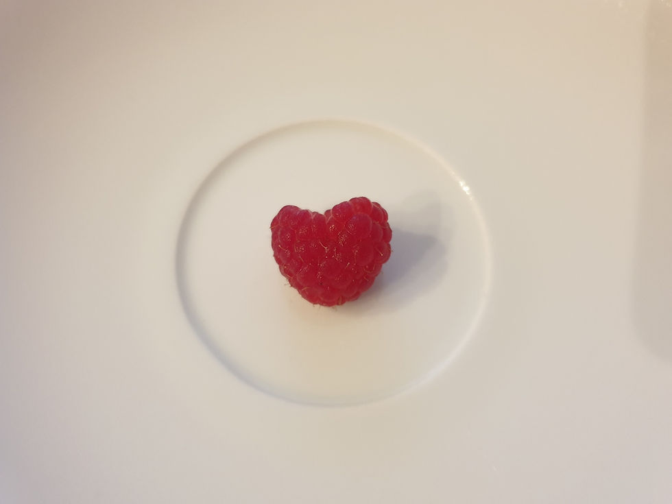 Eine Himbeere in Herzform liegt auf einem weißen Teller