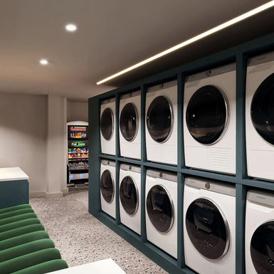 Modern laundry room, numerous washing machines, green seating, Imperial College London accommodation.