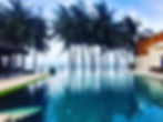 Infinity pool that reaches over a beach, with palm trees