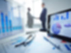 Business charts and data on screen with professionals shaking hands in background