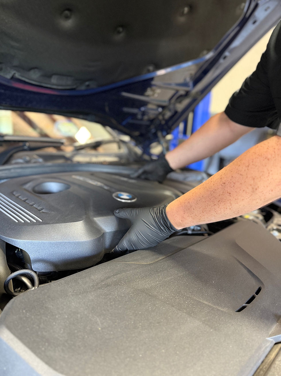 Apprentice Will Kendall working on a BMW in view are his gloved hands and arm