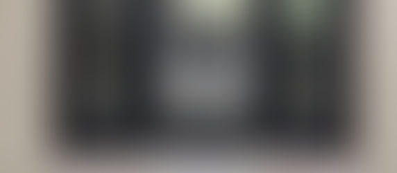 Black custom iron entry door with a patterned glass. Tiled path, and plants surround the entrance. Blue sky above.