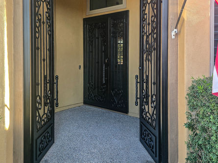 Custom iron courtyard enclosure open to a black double security door, creating a welcoming atmosphere.