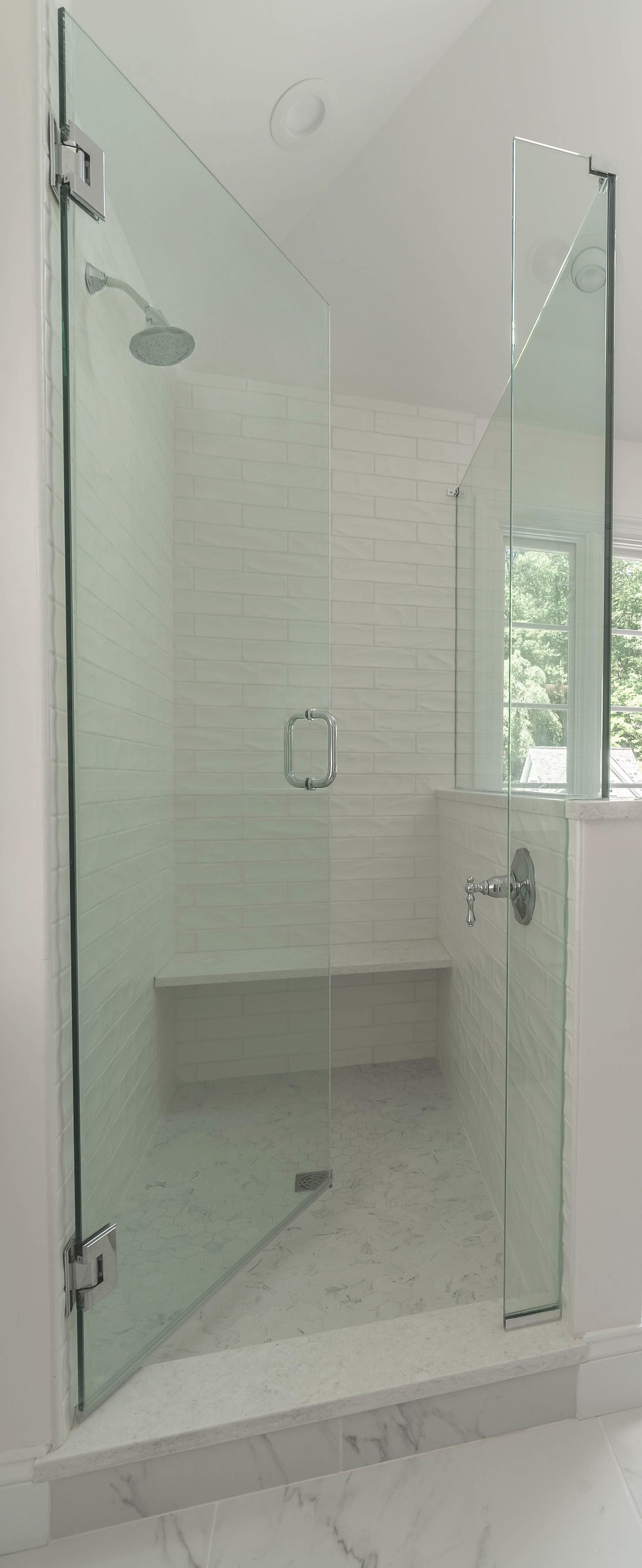 Minimalist walk-in shower with frameless glass door, white subway tile walls, built-in bench, and marble flooring