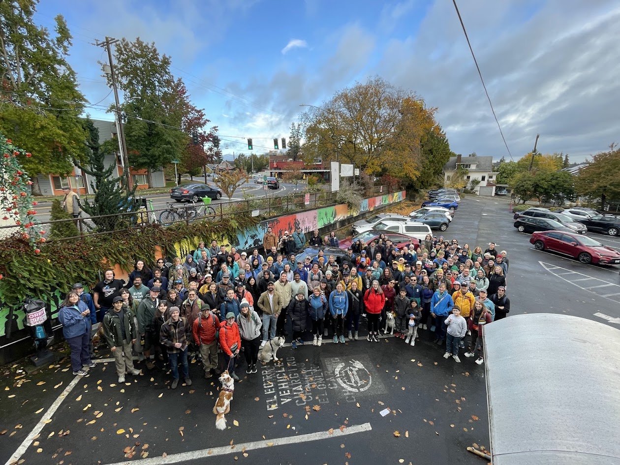 Walkers posing for a group photo in a parking lot at the 2025 edition of this walk, then called the Phinney, Fremont and Ballard Fall Frolic.
