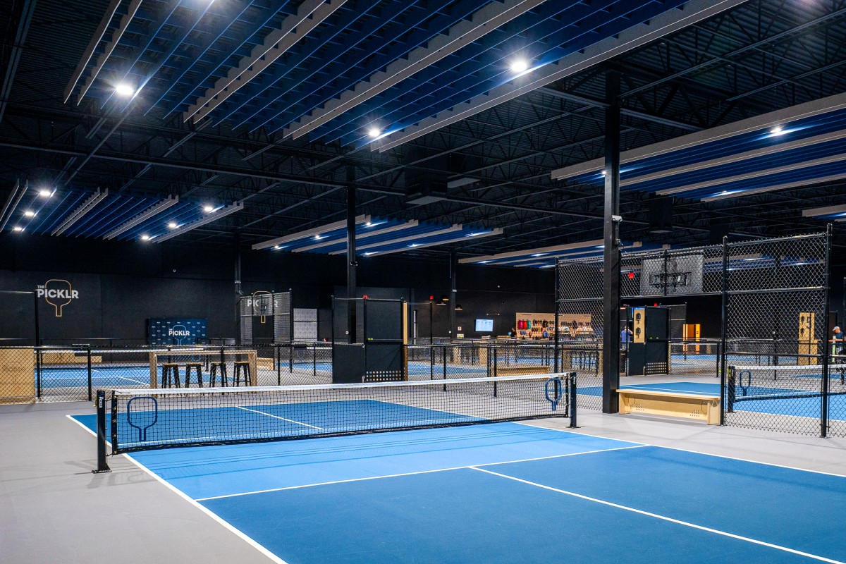 <h2>From Roasting Cacao to Ten Indoor Courts</h2>
<p>Walk into 124 North 35th Street in Fremont today and the smell of roasting cacao is gone, replaced by the pop of paddles on plastic balls across ten indoor courts. The brick building spent years as Theo Chocolate's organic, fair-trade roastery before the company moved on and left a 27,000-square-foot shell looking for a second life. In April 2026, The Picklr found one. Rajiv Khatri, the club's owner, described the opening as a turning point for the surrounding blocks, and framed the club less as a gym than as Fremont's third space, somewhere to be that isn't work or home. Ten courts inside a former candy factory is an unusual way to make that argument, and Fremont seems to be buying it anyway. Pickleball has spent the last few years turning into the fastest-growing sport in the country by most counts, driven by a low barrier to entry, a court a third the size of a tennis court, and a rally that rewards patience over power. Seattle's version of that boom just landed in one of its most recognizable buildings, a former factory that already had the scale and the industrial character the sport's biggest new clubs tend to look for.</p>
<h2>The Building's Other Life</h2>
<p>Theo Chocolate operated its roastery out of the Fremont building for years, the Organic and Fair-Trade Roaster signage still legible on the brick above the windows even as new tenants circulated through. Once the space sat empty, its 27,000 square feet made it one of the larger available footprints in a neighborhood that had mostly run out of room to build new. The Picklr's build-out kept the industrial bones, exposed structure and all, and filled the floor with regulation courts instead of roasting equipment. It is the kind of adaptive reuse Fremont has leaned on before, an old warehouse or factory finding a new purpose rather than getting torn down for something taller.</p>
<h2>Ten Courts and a Championship Court</h2>
<p>The finished club holds ten indoor courts, including one championship-sized court that is fully fenced for tournament play, plus outdoor-style surfacing throughout to match the feel players get on a municipal court outside. A pro shop stocks paddles and gear for anyone who shows up without their own, and a private event space rounds out the building for group bookings, corporate outings, or a birthday party that wants something more active than a bowling alley. League play, open play, and tournaments all run through the same ten courts, alongside private and semi-private lessons taught by certified trainers for players who want structured coaching rather than a pickup game.</p>
<h2>Opening Weekend</h2>
<p>The Picklr Fremont opened to the public on Saturday, April 4, with a grand opening that ran from 11 a.m. to 4 p.m. and offered free all-day play to anyone who walked in. The day mixed pro play sessions and instructional clinics with catered food and drinks, raffles and prizes, and, in a detail that says something about the sport's reputation for joint-friendly, all-ages appeal, on-site chiropractic services. It was as much a neighborhood open house as a ribbon cutting, built around getting as many first-time players onto the courts as possible before the club's regular schedule took over.</p>
<h2>A National Franchise Landing in Fremont</h2>
<p>The Picklr itself is barely five years old, founded in 2021 in Uintah, Utah, by Jorge Barragan, and it has grown fast enough since to call itself North America's fastest-growing pickleball franchise. More than 500 locations have been sold across the United States, Canada, and Japan, though only a fraction are open and running at any given point, since new clubs take time to build out after a franchise agreement gets signed. That gap between locations sold and locations open is itself a sign of how far ahead of supply the demand for indoor courts has run. Fremont marks The Picklr's third Washington location, following clubs in Federal Way and Tacoma, and its scale, ten courts and 27,000 square feet, positions it as something closer to a flagship for the region than a standard-issue franchise outpost.</p>
<h2>What Membership Costs</h2>
<p>Pricing runs in tiers by age and access level. A junior membership for players 5 to 17 runs $74 a month, while a standard play membership sits at $109 a month. Adult unlimited access costs $141 a month, and a family unlimited plan, covering two adults and up to four juniors, runs $308 a month. Day passes and drop-in rates exist for anyone who wants to try a court before committing to a membership tier, a lower-stakes entry point for a sport most people learn by simply showing up and hitting a few balls.</p>
<h2>Fremont's Third Space</h2>
<p>Whether The Picklr becomes the neighborhood hangout Khatri describes will come down to whether people actually treat it that way, showing up between matches to sit at the pro shop counter or linger after a lesson rather than leaving the moment their court time ends. The building has already made one identity switch, from a chocolate roastery with its name still cut into the brick to a pickleball club with ten courts and a waitlist for prime-time slots. Fremont has absorbed stranger transformations than that. This one just happens to come with paddles.</p>