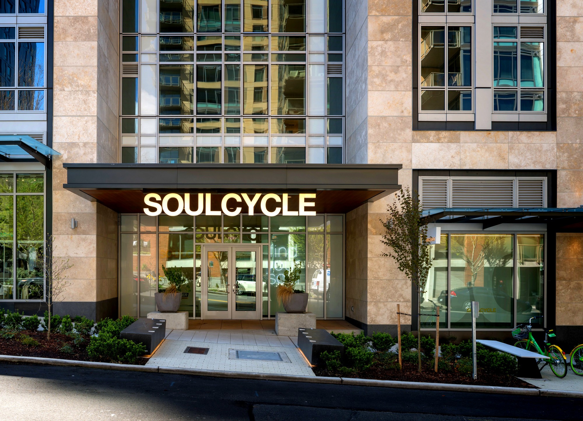 <h2>The Same Candlelit Ride, Nineteen Years Later</h2>
<p>SoulCycle started in 2006 in the rear lobby of an old dance studio on Manhattan's Upper West Side, a space Elizabeth Cutler and Julie Rice found on Craigslist after Ruth Zukerman, who had already been teaching spin in the city for a decade, introduced the two over lunch. The first class rode on April 15, 2006, on West 72nd Street. Two decades later, the format has spread far enough that it now fills a glass-fronted retail space inside a South Lake Union residential tower at 2105 9th Ave, on the edge of Denny Triangle, running the same candlelit, music-driven ride the company built its name on. The Seattle studio keeps the brand's formula intact: dim rooms, a stacked platform up front, and class themes that turn a workout into an event. Fuego Friday runs a Latin-music ride. Taylor Swift + Friends builds an entire class around one artist's catalog. SoulSurvivor rounds out a schedule led by a roster of local instructors, Kolten, Stephanie P., Jess L., Victoria H., Evan, Earl, and Jenna among them, each bringing a different music sensibility to the same forty-five minutes on a bike.</p>
<h2>From a Craigslist Lobby to a National Format</h2>
<p>The founding story matters here because SoulCycle's whole pitch rests on it: three women who couldn't find the level of energy and community they wanted in New York's cycling studios built one themselves, starting small enough that the first location was borrowed space in someone else's dance studio. That scrappy origin is easy to forget standing inside a studio built into a modern glass tower, but the format itself hasn't drifted far from the original idea, a coach-led ride set to music, in the dark, meant to feel more like a shared experience than a workout class. Cutler and Rice were both mothers who had relocated to Manhattan, one from Los Angeles and one from Boulder, and neither had a fitness-industry background before SoulCycle. That outsider's perspective shaped the format as much as Zukerman's decade of spin-teaching experience did, favoring atmosphere and music over the technical drills a longtime instructor might have defaulted to.</p>
<h2>The Studio on 9th Avenue</h2>
<p>Seattle's location sits at 2105 9th Ave, inside a residential high-rise near the Denny Triangle and South Lake Union border, close enough to both neighborhoods that listings split on which one to credit. The studio's own entrance carries the brand's signature look: a lit yellow SOULCYCLE wordmark on a white wall, a single bike parked near reception, and a retail wall stocked with branded apparel, from graphic tees to a Nike collaboration tank. It reads less like a gym lobby and more like a small boutique that happens to have bikes in the back rooms. The building itself sits among the newer glass residential towers that have reshaped this stretch of 9th Avenue over the past decade, part of the broader wave of development that turned Denny Triangle from a mostly industrial gap between downtown and South Lake Union into one more dense residential corridor.</p>
<h2>Not Just Spin: Themed Rides</h2>
<p>What separates SoulCycle from a standard indoor cycling class is how much of the schedule gets built around a specific mood rather than a generic difficulty level. Fuego Friday leans into Latin music for a faster, hip-driven ride. Taylor Swift + Friends turns a pop catalog into forty-five minutes of choreography-adjacent cycling, the kind of themed class that shows up on social media as often as it shows up on the studio calendar. SoulSurvivor closes out the week with a format built around endurance rather than a single artist's songbook. Instructors rotate through all three, which means the same class name can feel different depending on who's teaching it that day, a deliberate feature of the format rather than an inconsistency.</p>
<h2>What a Ride Costs</h2>
<p>SoulCycle's pricing runs on a national structure that generally holds across markets: a single drop-in class runs somewhere between $25 and $42 depending on demand and time slot, a five-class pack lands around $175 to $195, and monthly membership plans range from roughly $134 to $481 depending on how many classes are included and whether the plan auto-renews. None of those figures are Seattle-specific promises, since SoulCycle prices shift by studio and season, but they give a realistic range for what a South Lake Union rider should expect to pay before ever checking the app.</p>
<h2>Nineteen Years In, Still the Same Bet</h2>
<p>What's actually notable about the Seattle studio isn't that it exists, indoor cycling studios are common enough in a city this size, it's that the format hasn't needed to change much to keep filling a room nineteen years after two moms and a longtime spin instructor decided New York needed something better than what was already out there. The lobby swapped a rented dance studio for a glass tower on 9th Avenue, and the retail wall has grown from nothing into a full apparel line, but the bet underneath all of it, that people will pay for a ride built around music and community rather than just cardio, is exactly the one Cutler, Rice, and Zukerman placed in 2006.</p>