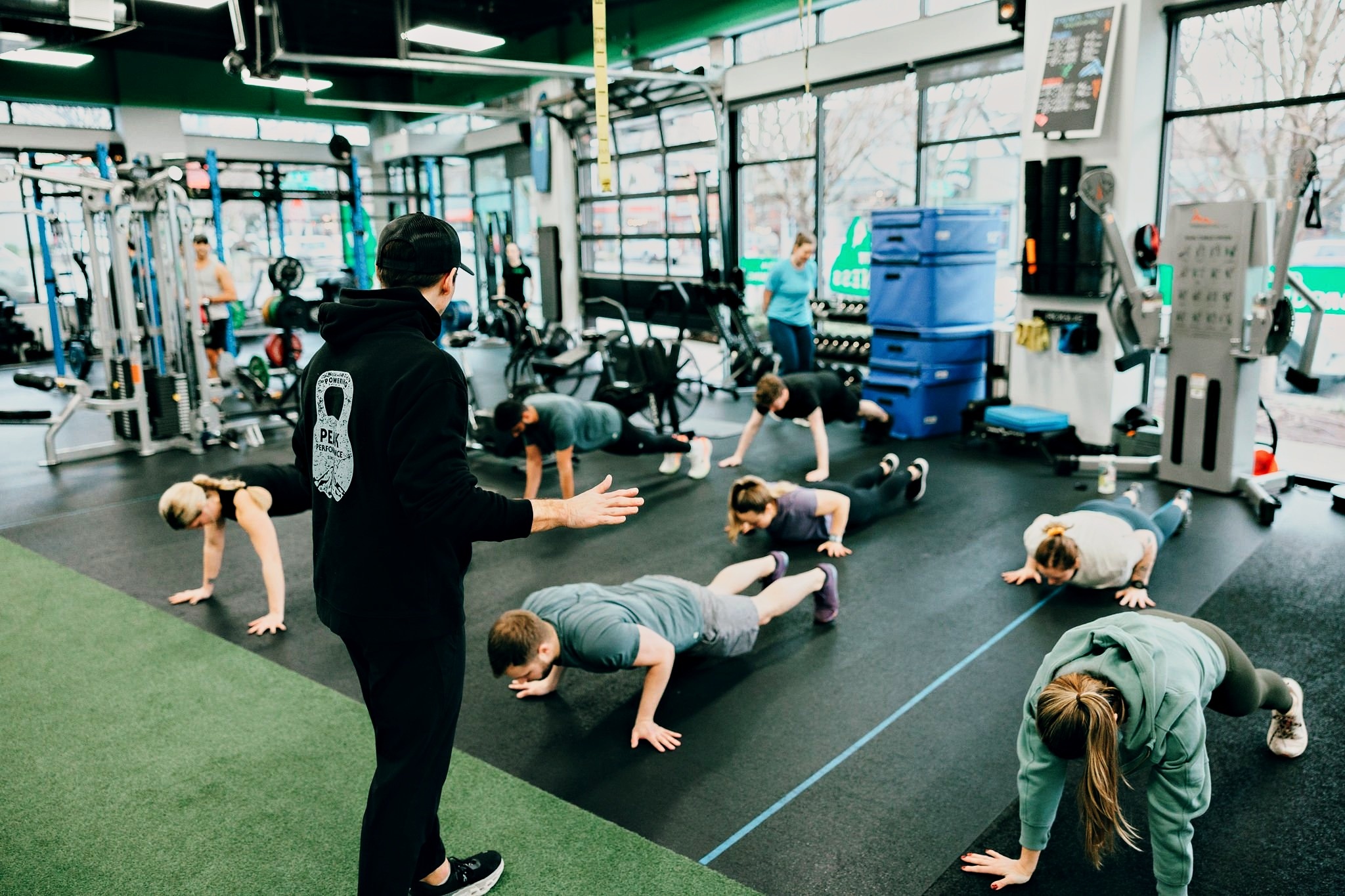 A coach talks a Northwest Fitness Project group class through a plank circuit across the gym floor.