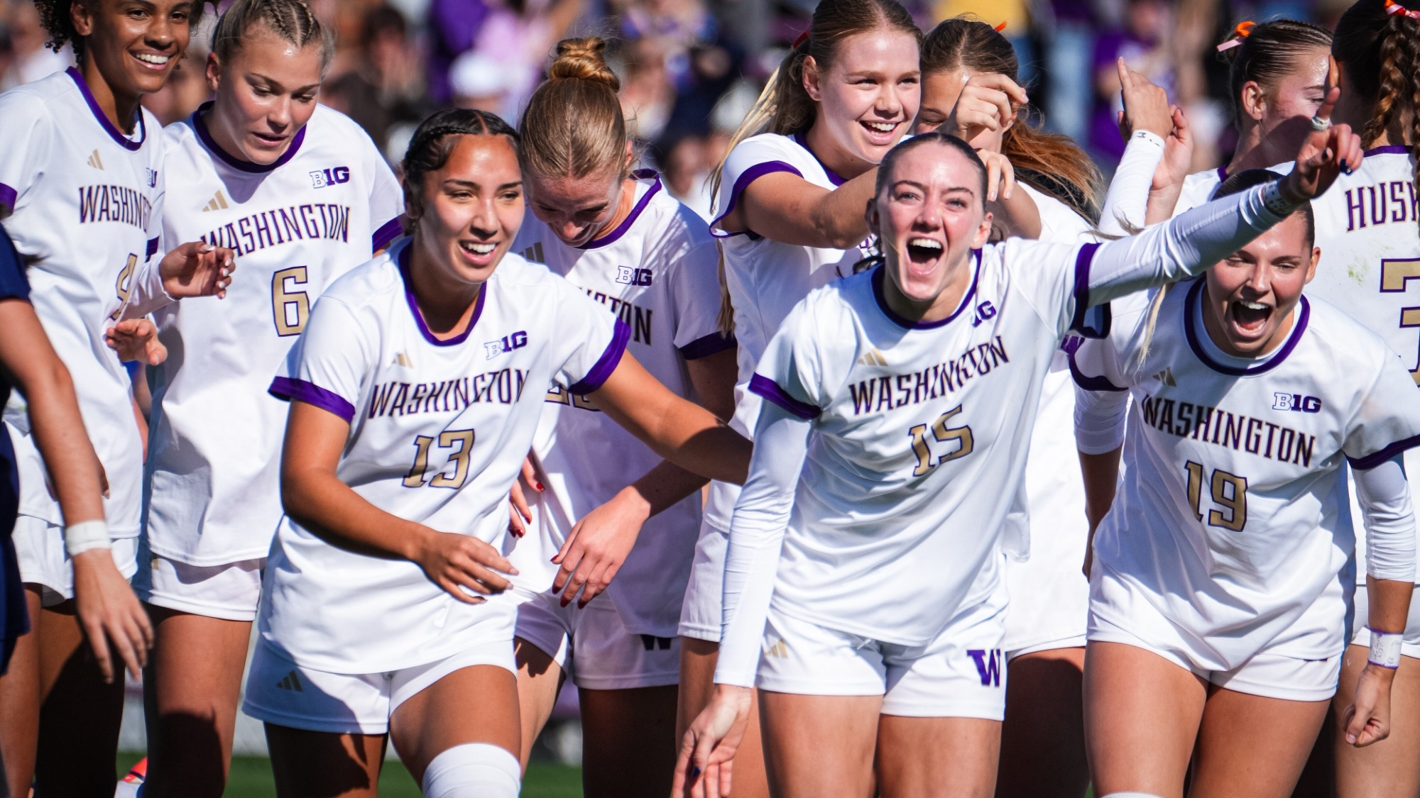 Washington players in white home kits (#15, #19, #13) celebrating in front of a purple-clad Husky crowd during the 1-0 win over Penn State at Husky Soccer Stadium, October 11, 2026; UW Athletics' own photo from its match recap