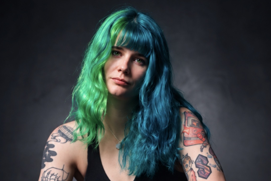 Sammie Brown, owner of RowdyBox, in a studio portrait with tattooed arms and green and blue hair