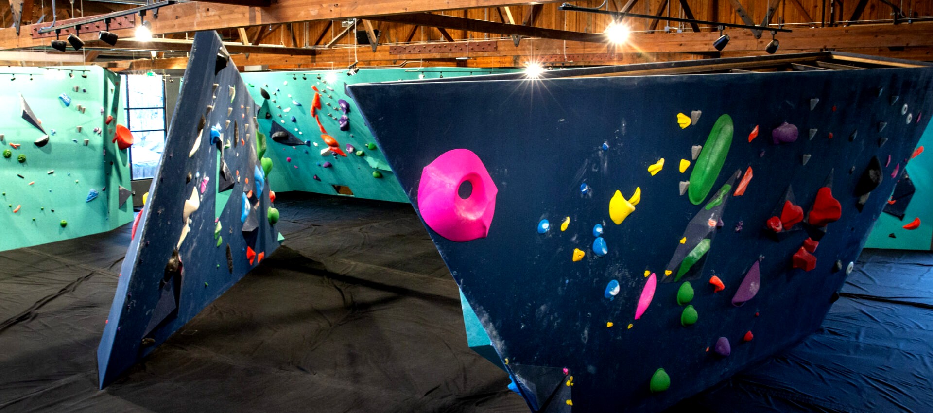 <h2>From a Warehouse Floor Test to Eight States</h2>
<p>In the spring of 2011, Andy Wyatt and Chris Potts filled two empty rooms of a Central District warehouse with as many climbing walls and boulder problems as they could build, then tested whether the foam floor would actually catch a fall by leaping off the gym's own staircase. That warehouse became Seattle Bouldering Project. Fourteen years later, the company Wyatt and Potts started by throwing themselves at their own flooring runs thirteen gyms across eight metro areas, and Seattle is still where the walls get designed. Two of those gyms sit one block apart in Fremont, painted in the teal, green, and navy that has become the brand's signature, and they are the reason most Seattlites think of Fremont, not the Central District, when they hear the name. That's a small mix-up worth clearing up, because the real story is bigger than either building. A gym born from two people testing their own foam floor now has outposts in Austin, Minneapolis, Salt Lake City, Brooklyn, Boston, Washington DC, and Tempe. None of that happened by accident, and Fremont's colorful walls are as good a place as any to see what a hometown company looks like after it stops being small.</p>
<h2>The Original Is in the Central District, Not Fremont</h2>
<p>The founding gym, now known as Poplar, still stands at 900 Poplar Pl S, in an ex-warehouse overlooking I-90 that has since grown a yoga studio, a cafe, and a full weight room around its original bouldering walls. Fremont and Upper Walls came later, as Seattle Bouldering Project expanded within its own city before it ever left Washington. The company's own website puts it plainly: this is where Bouldering Project got its start, calling Seattle its hometown and the place it found its groove designing walls and building community. Three Seattle locations exist today, Poplar, Fremont/Upper Walls, and University District, and a single membership moves between all of them.</p>
<h2>Two Buildings, One Block, All Color</h2>
<p>Fremont sits at 3535 Interlake Ave N, and Upper Walls sits one block north at 3625 Interlake Ave N, close enough that the walk between them runs about sixty seconds. Fremont carries the bigger footprint and the neighborhood's flair, a bright two-floor space combining bouldering, fitness, and co-working under one roof. Upper Walls is smaller and more focused, a dedicated bouldering and training space tucked into the block behind it. Fremont is open weekdays from 6 a.m. to 10 p.m. and weekends from 7 a.m. to 10 p.m., while Upper Walls runs 9 a.m. to 9 p.m. every day. The teal and green walls, hung with fluorescent pink, yellow, and orange holds, are less a design choice than a way of making an industrial building feel like it belongs to the neighborhood outside it.</p>
<h2>More Than a Wall</h2>
<p>None of the three Seattle gyms sells bouldering alone. Fremont and Upper Walls both run a dedicated yoga studio with a full class schedule, a functional fitness space stocked with free weights and racks, and a gear shop for anyone who shows up without shoes or chalk. Co-working spaces round out the building, turning a climbing gym into somewhere a member might reasonably spend an entire workday, not just an hour on the wall. First-timers can rent shoes at the desk rather than buy a pair before they know if the sport sticks, a small detail that keeps the barrier to a first visit low.</p>
<h2>From Seattle to Eight States</h2>
<p>Growth came fast after that first warehouse. Austin was the second location, opened by the same founders, followed by Minneapolis before the original ownership group sold the company during the pandemic. The new owner kept building, adding Brooklyn, Boston, Dallas, Salt Lake City, and Washington DC before opening in Tempe, Arizona. Thirteen gyms now carry the Bouldering Project name, and every one of them traces back to two people testing a foam floor in a Central District warehouse that had nothing in it yet. Seattle's three locations remain the company's proof of concept, the market where a design gets tried before it ships anywhere else.</p>
<h2>What It Costs to Climb Here</h2>
<p>A single membership at any Seattle location runs $105 a month for adults 21 and up, with a one-time $55 activation fee. Younger climbers pay less: $95 a month for ages 14 to 20, and $75 a month for 13 and under, both carrying the same activation fee. Members can freeze a membership for $10 a month during a slow stretch, or cancel with no fee attached through the gym's online request process, a friendlier policy than most gyms offer. Day passes and ten-visit punch cards exist for anyone who wants to try the walls before committing to a monthly rate.</p>
<h2>The Walls That Started It</h2>
<p>This fall's Bouldering League runs out of the University District gym, from the week of September 29 through October 30, open to any member with access across all three Seattle locations, Fremont included. It is a small, ongoing reminder that Seattle Bouldering Project never stopped being a local company, even after its name showed up in eight states. The staircase Wyatt and Potts jumped from in 2011 is long gone, replaced by three buildings' worth of teal and navy walls loaded with color, but the instinct behind it, test it yourself before asking anyone else to trust it, still shapes every gym the company opens.</p>
