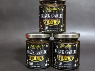 Three jars of Chili & Valley Black Garlic Chutney stacked on each other.