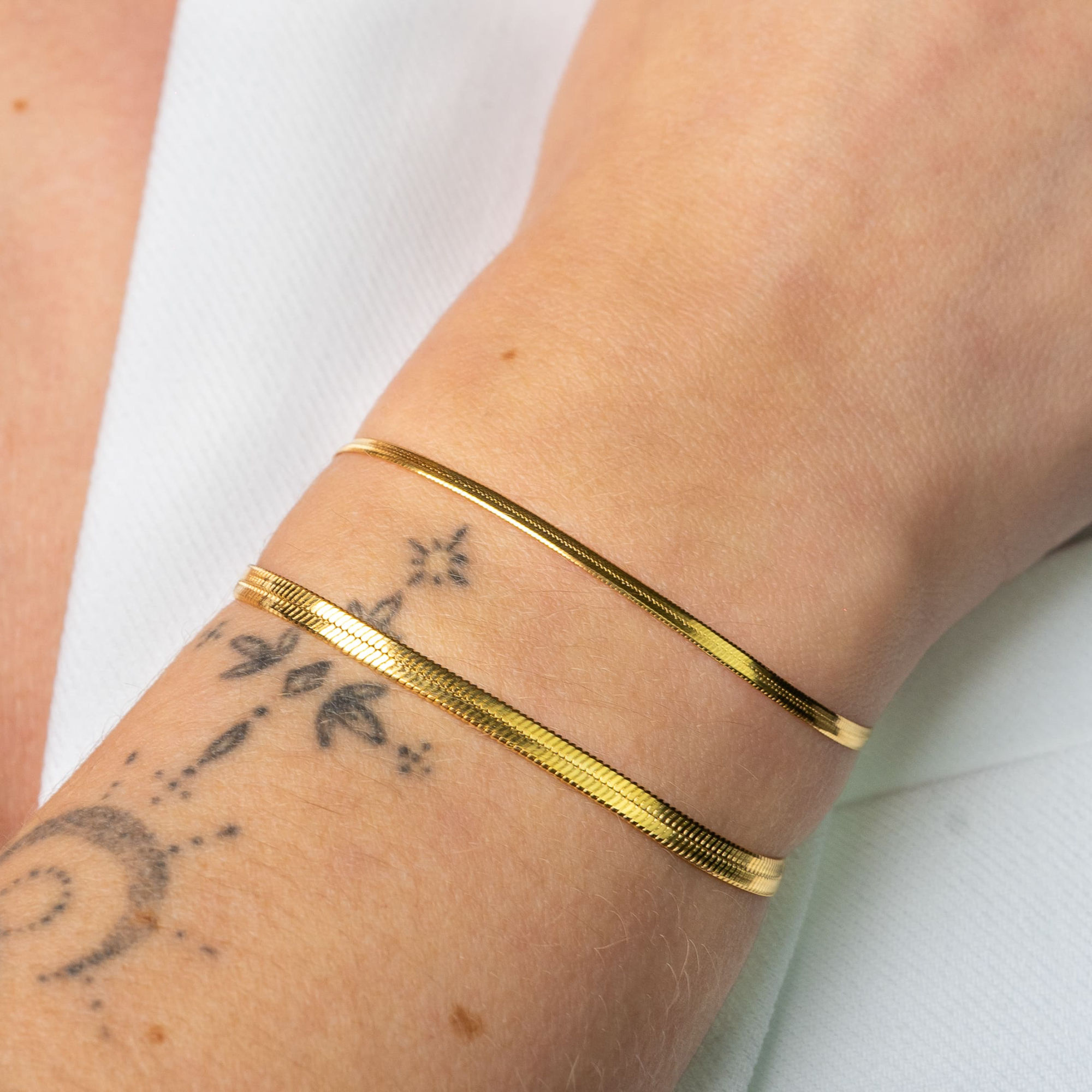 Bracelets en maille serpent dorée portée sur poignet tatoué