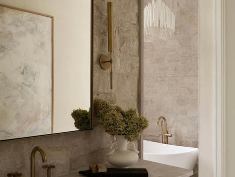 Elegant bathroom design with warm brass fixtures, natural stone wall, freestanding tub, and soft neutral tones creating a cohesive and inviting atmosphere.