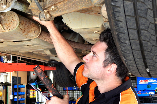 Mechanic inspecting the underside of a vehicle on a hoist