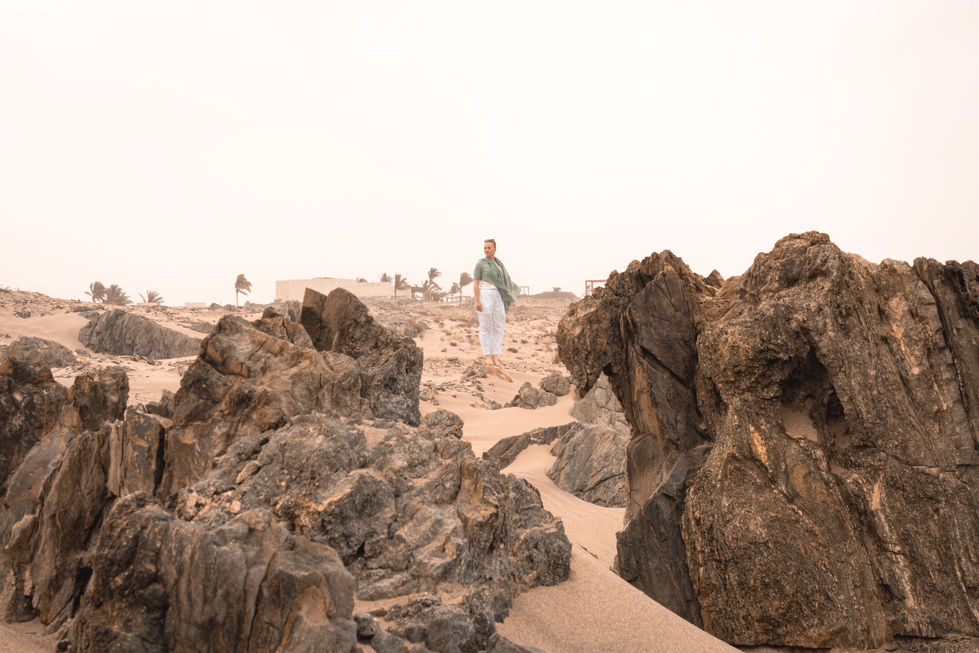View across rugged volcanic rocks with a distant figure exploring the desert landscape near Alila Hinu Bay.