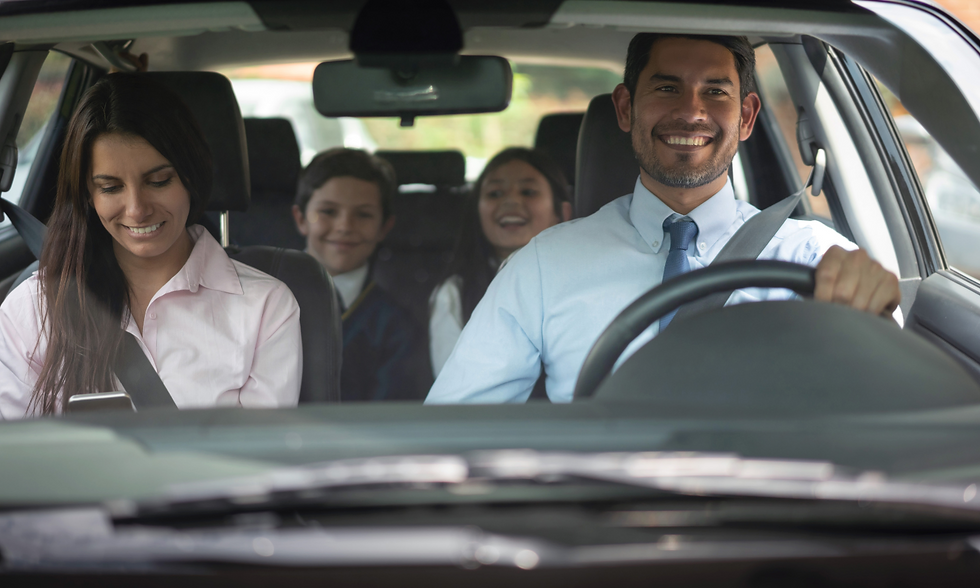 A family of four in a car, with the father driving and smiling, the mother looking at her phone, and two children in the backseat, laughing, capturing a happy family outing.