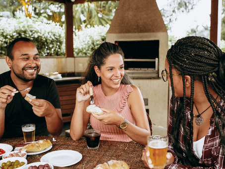 Three adults sit together at an outdoor table, laughing and talking while sharing food and drinks, illustrating a candid moment of human connection.