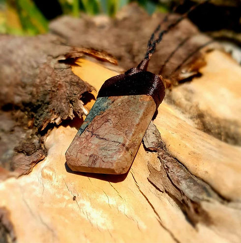 Hand carved Jasper pendant resting on mossy wood, showing warm pink and grey tones — symbolising the grounding, earthy energy of New Zealand Jasper.