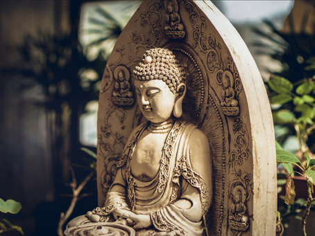 Buddha statue with ornate carvings, sitting peacefully amidst green plants. Soft lighting casts a serene, contemplative mood.