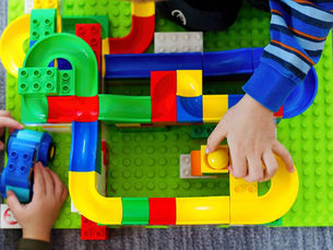 Hands of two young children playing with set of colourful building block ball run. Photo taken from above.