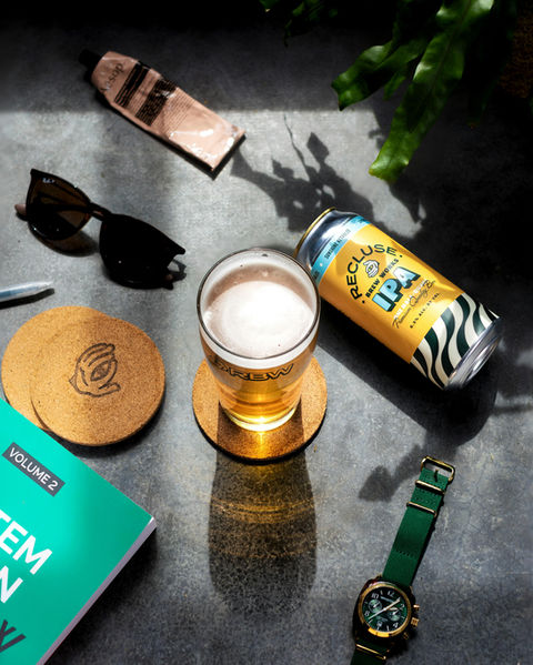 Recluse IPA beer in glass, coasters, sunglasses, watch, and book