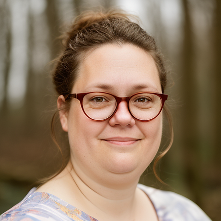 Middle aged woman of European ancestry with brown hair and brown eyes, smiling with mouth closed and wearing red glasses. Her hair is pulled up away from her face.